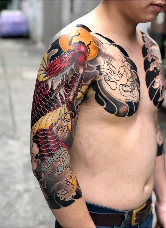 Người đứng nghiêng, để lộ hình xăm rồng màu sắc trên cánh tay và ngực, nền là con đường mờ nhạt.